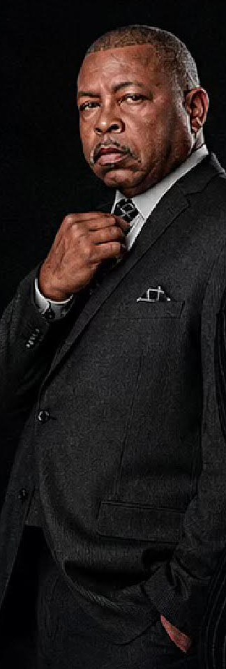 Cast member in a dark suit, straightening his tie