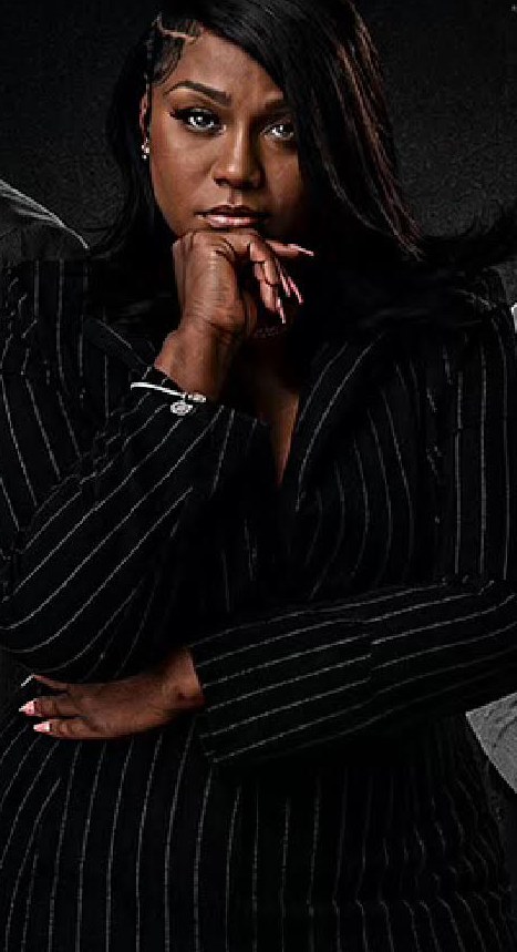 Cast member in a pinstripe suit, chin resting on her hand