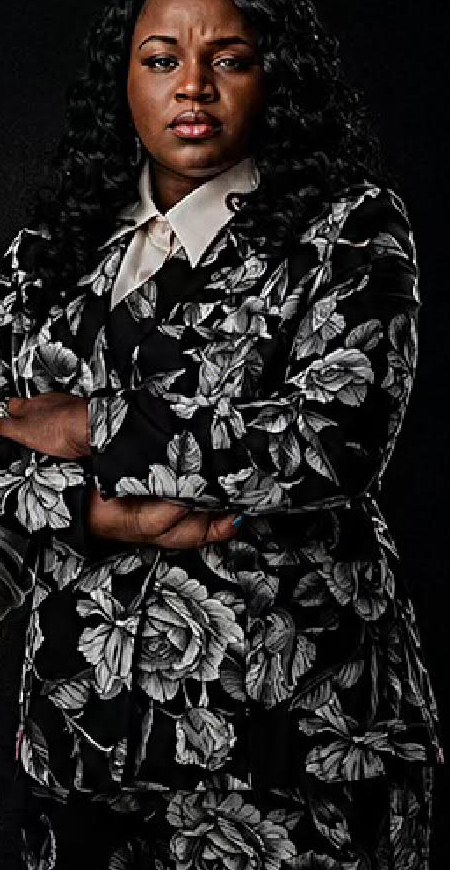 Cast member in a floral blazer, arms crossed